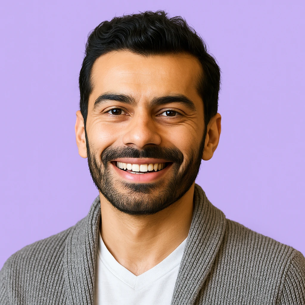 A smiling man with a beard and dark hair is wearing a gray sweater and white shirt. The background is a solid lavender color, conveying a cheerful tone.
